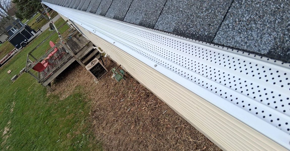 Close aerial view of a white perforated gutter cover installed at a roof edge above a yard